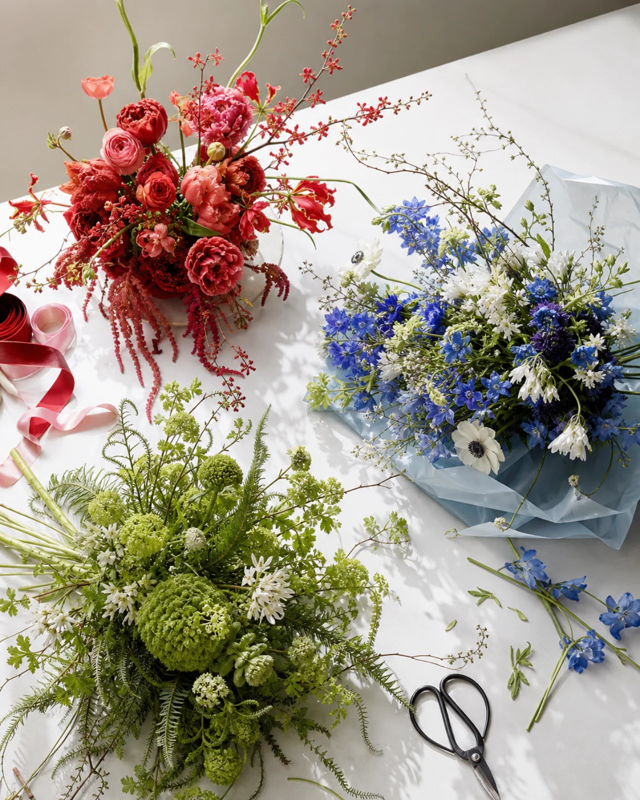 Três composições florais contemporâneas em vermelho, azul e verde sobre uma mesa branca